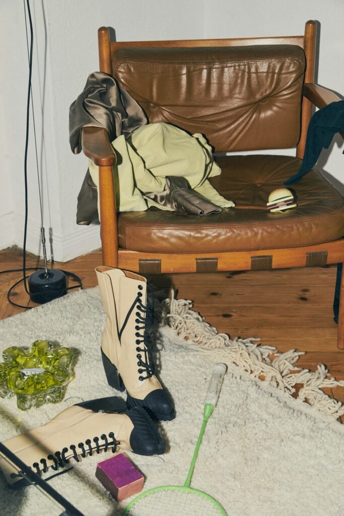 A messy corner of the room with a leather chair and clothes strewn all around