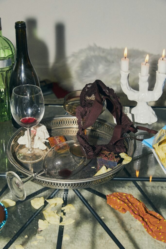 A glass table with a lit candelabra and a vintage tray littered with half empty glasses of wine.