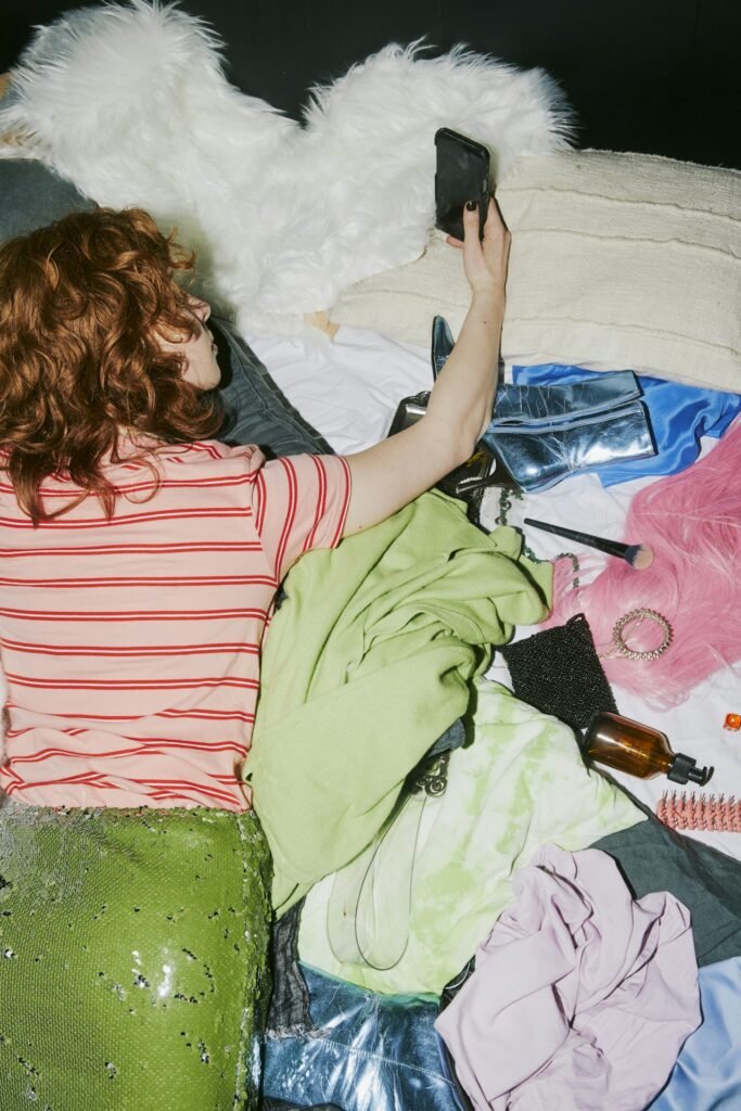A teen laying on their belly on the couch in a pile of clothes and makeup