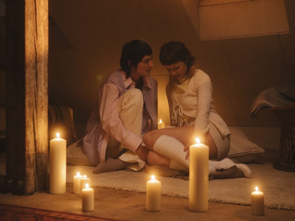 Two women sitting within a circle of candles in a dimly lit room.
