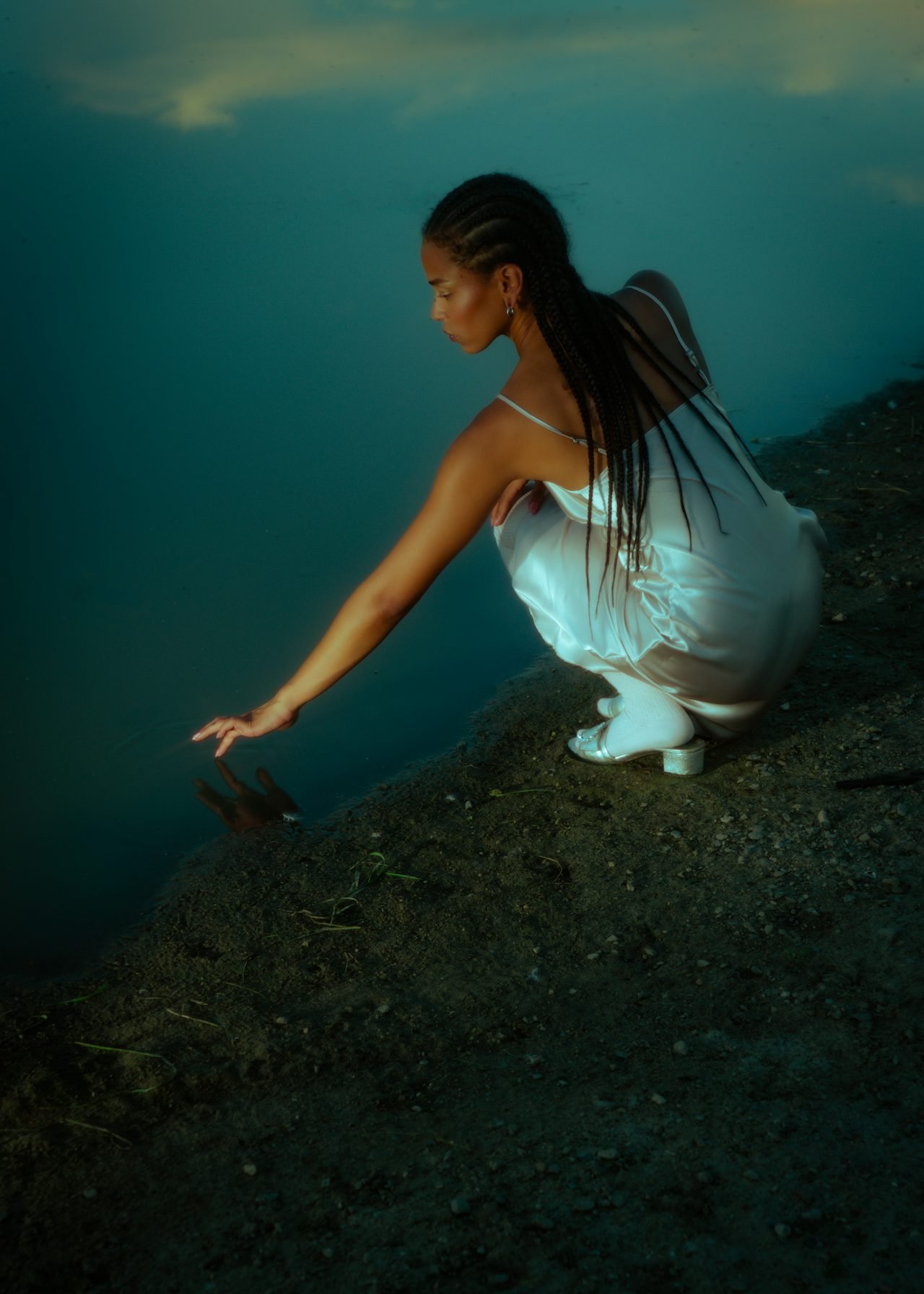 Woman of colour sitting by a creek and dipping her finger into the water