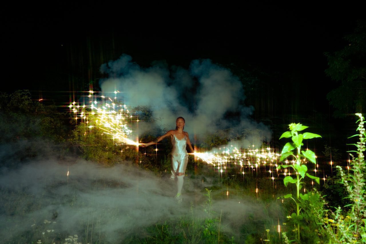 Woman of colour running through the dark with sparklers