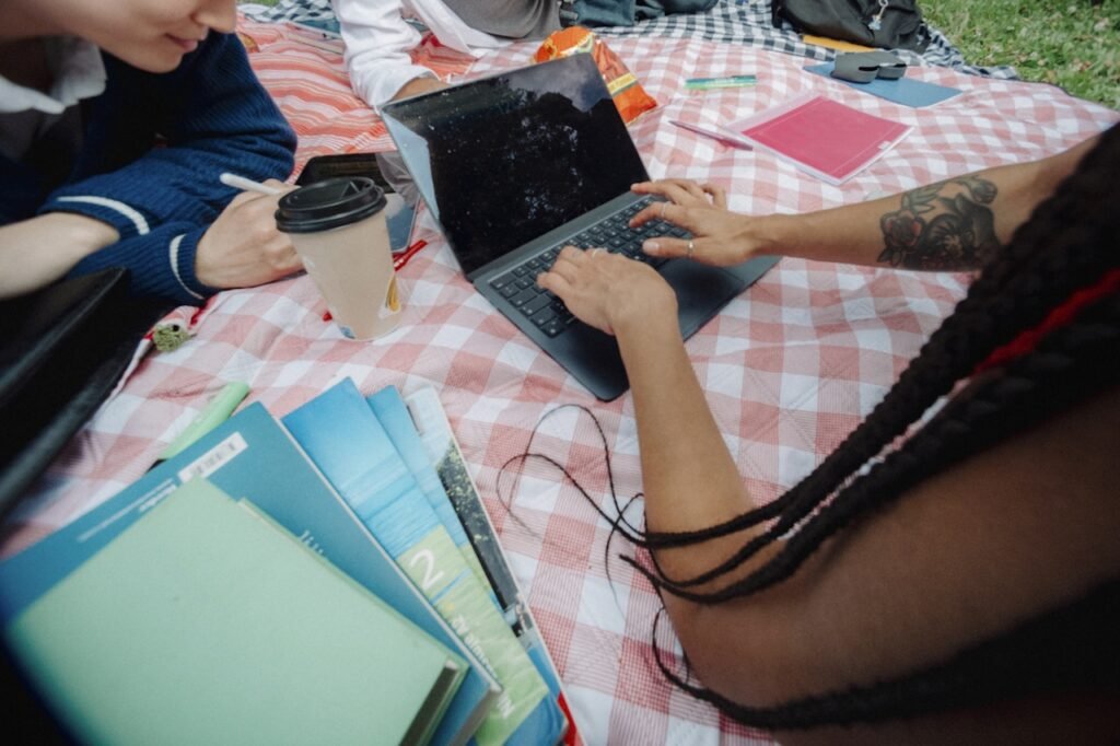 A WOC sitting on a picnic blanket with her laptop