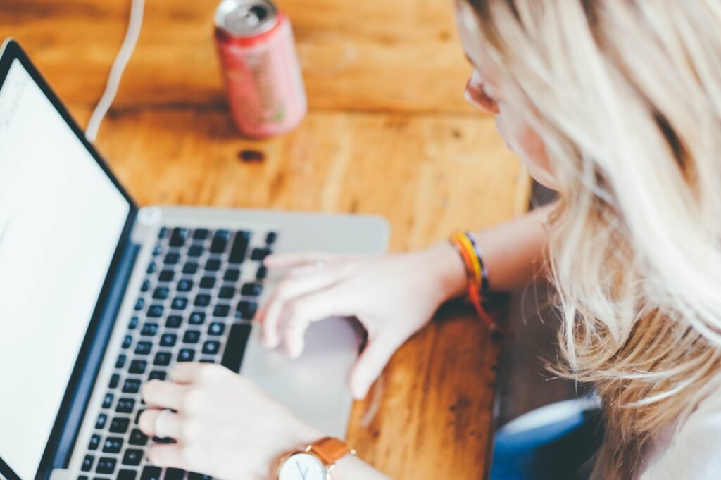 A woman sitting at a table working on her laptop next to a canned beverage