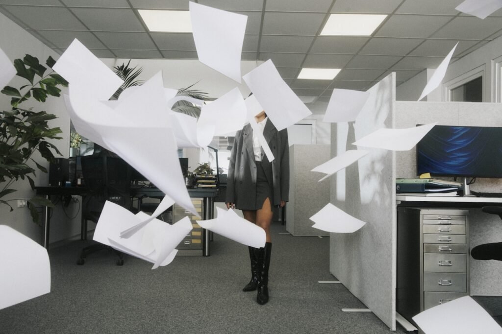A woman in an office setting with her face obscured by flying papers.