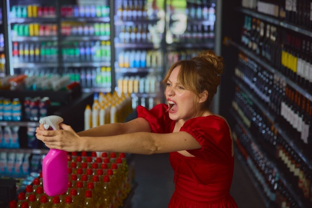 A very chicly dressed woman in a grocery store aggressively aiming a spray bottle.