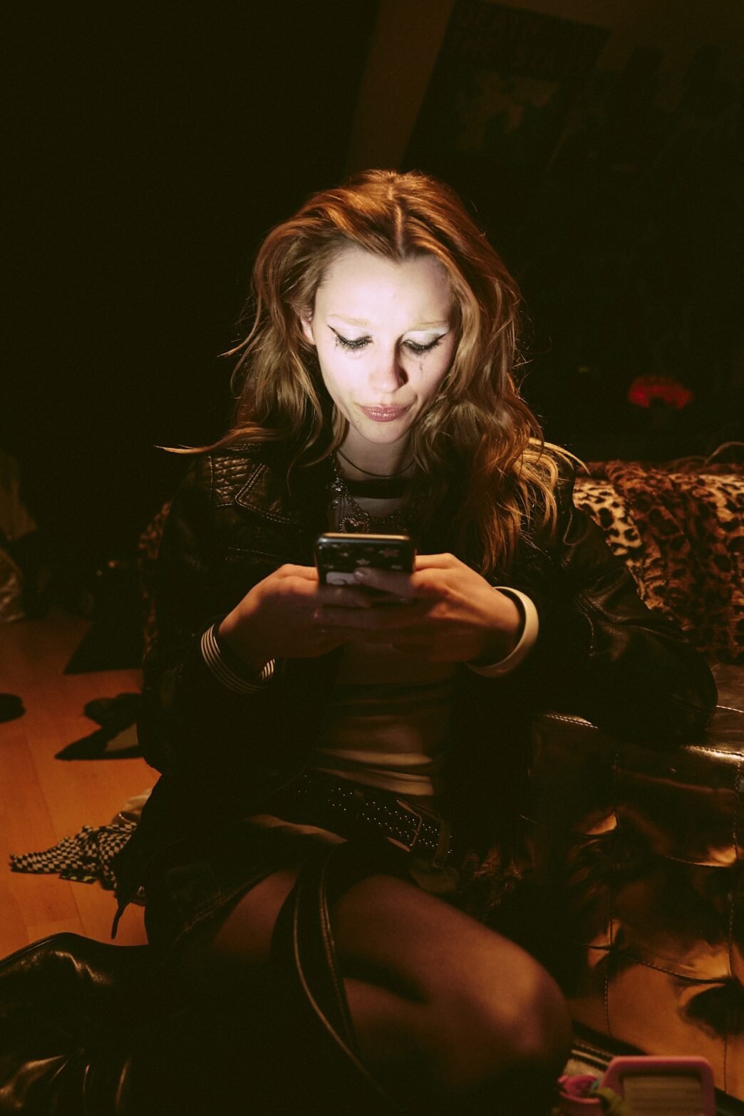 A woman in a dimmed room with the light of her phone illuminating her face.