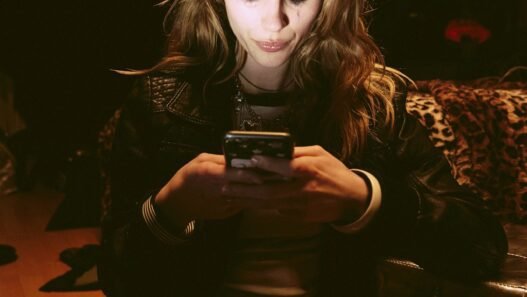 A woman in a dimmed room with the light of her phone illuminating her face.