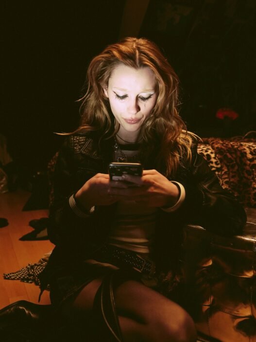 A woman in a dimmed room with the light of her phone illuminating her face.
