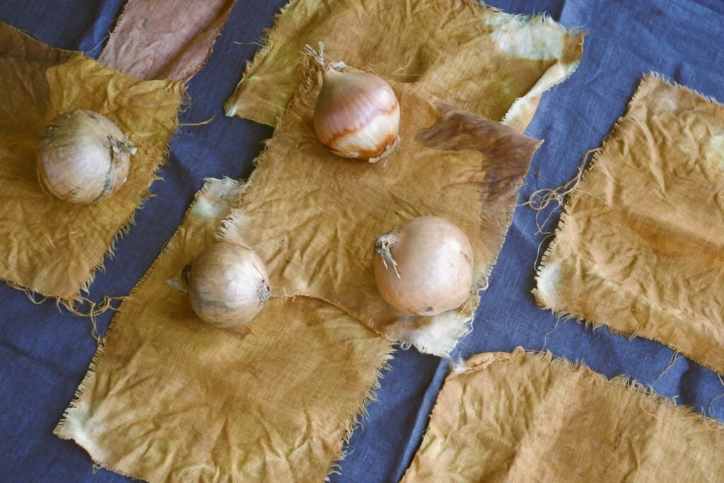 Onions sitting on fabric swatches that have been dyed using onion skins on an indigo surface.
