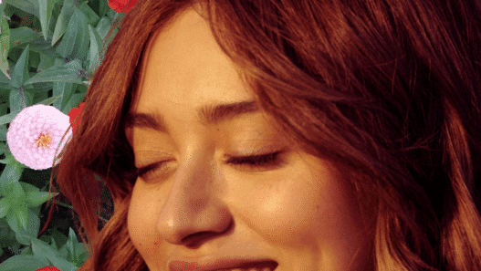 A young woman with the sun on her face and a collaged backdrop of flowers