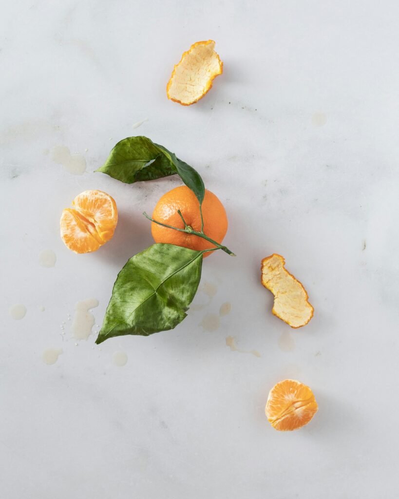 A orange surrounded by slices and peels on a marble countertop.