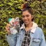 Bratty Bre wearing a demin jacket in front of a mossy green hedge holding a collection of zines.