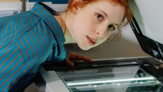 A red headed women with her face hovering above a photocopy machine.
