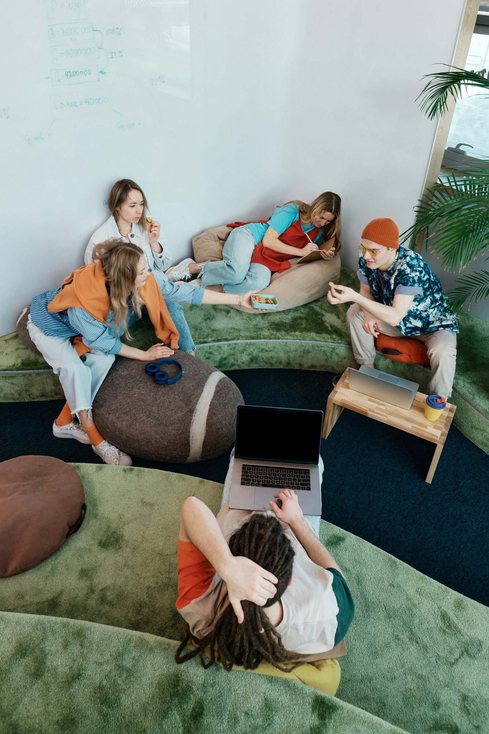 A group of 5 people sitting on comfy couches and chairs collaborating on a project.