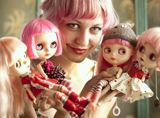 A female with super cool pink hair showing off her collection of customized Blythe dolls.