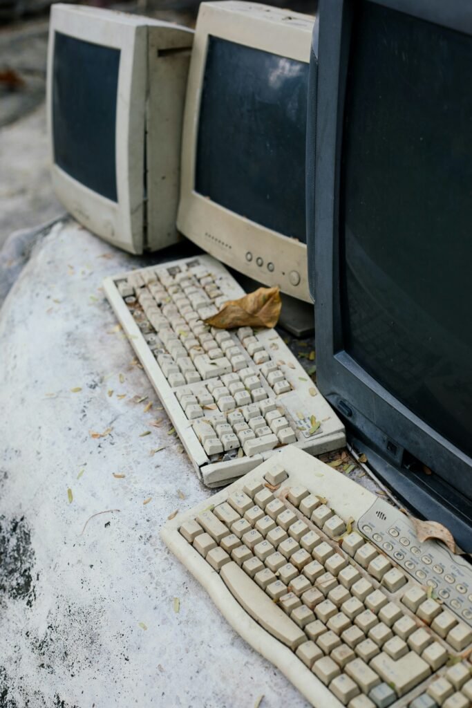 Three ancient computer monitors and two old keyboards in a state of disrepair.
