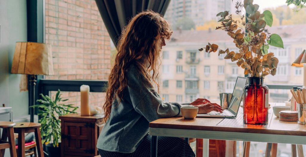 A woman in her bedroom sitting at a desk in front of a computer.