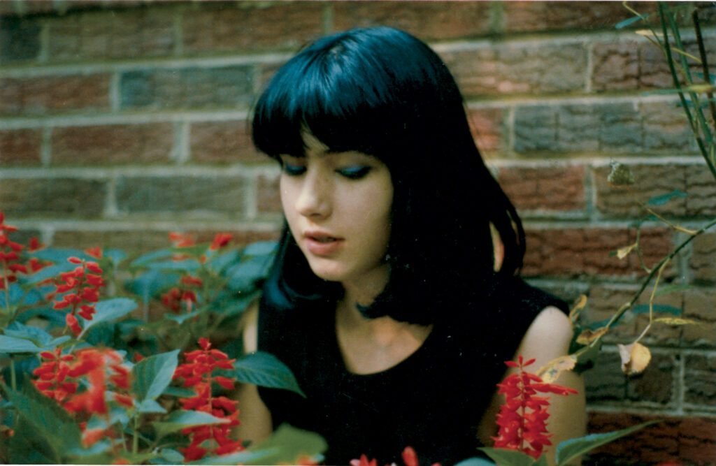 A 16-year old Kathleen Hanna sitting in a garden and smelling blossoms