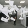 A woman standing in a blizzard of papers flying in the air in an office setting.