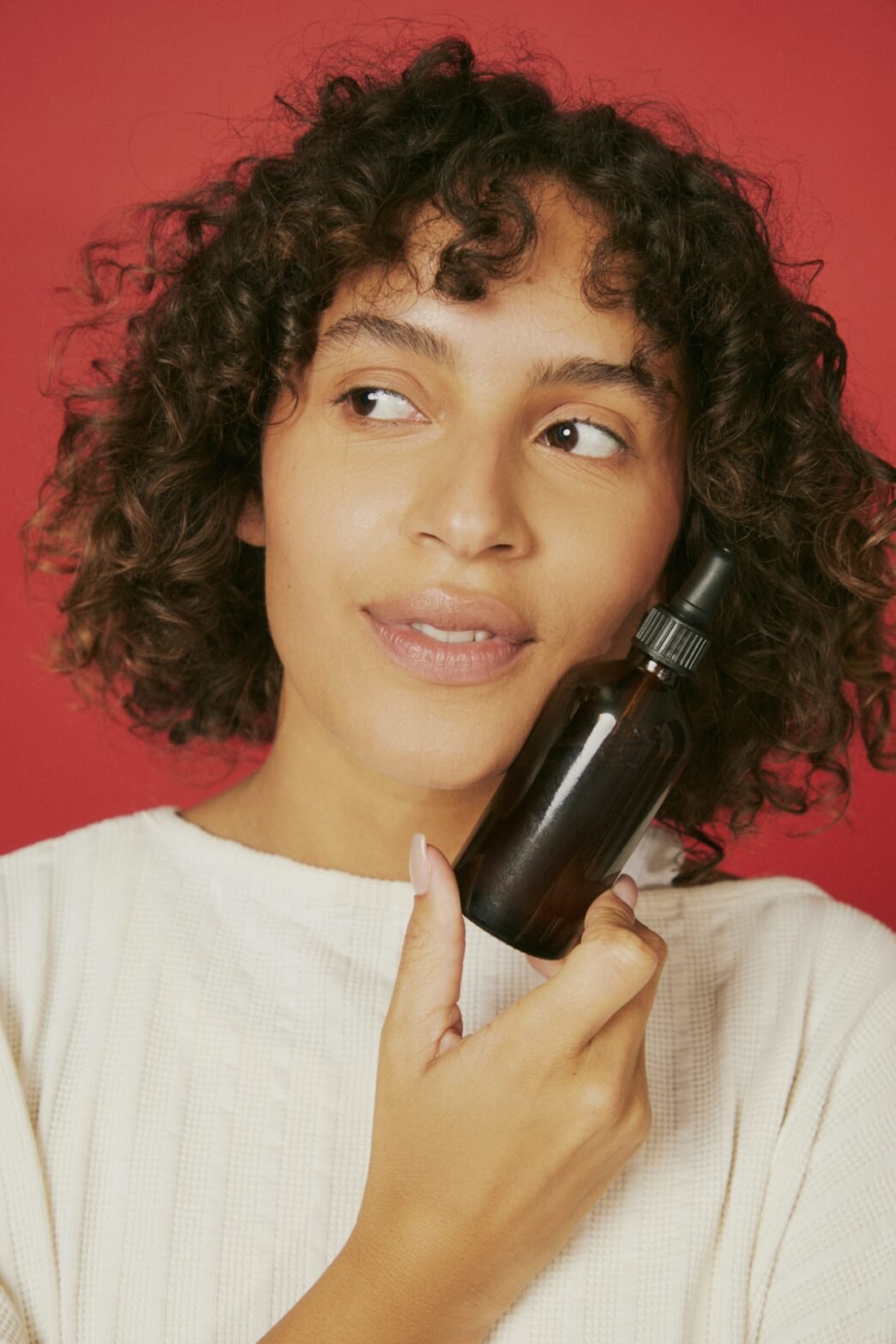 A person poses against a red background with a facial product up against their cheek.