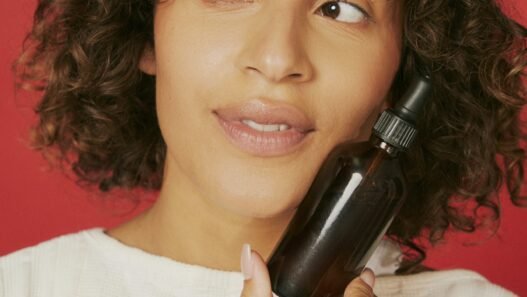 A person poses against a red background with a facial product up against their cheek.
