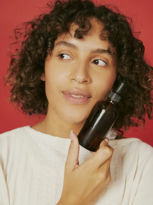 A person poses against a red background with a facial product up against their cheek.