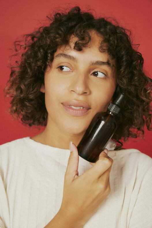 A person poses against a red background with a facial product up against their cheek.