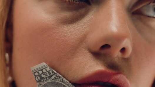 A blonde woman with a dollar bill held up against her cheek.