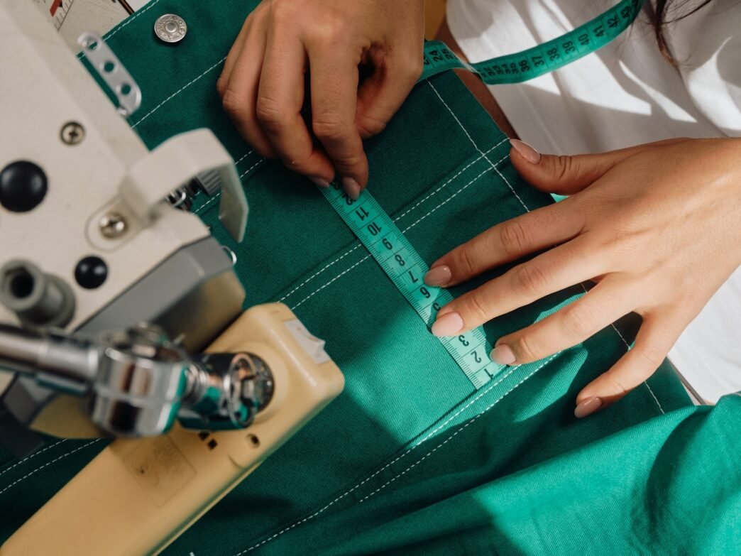 A person with a fabric measuring tape measuring a garment that they have in their sewing machine.