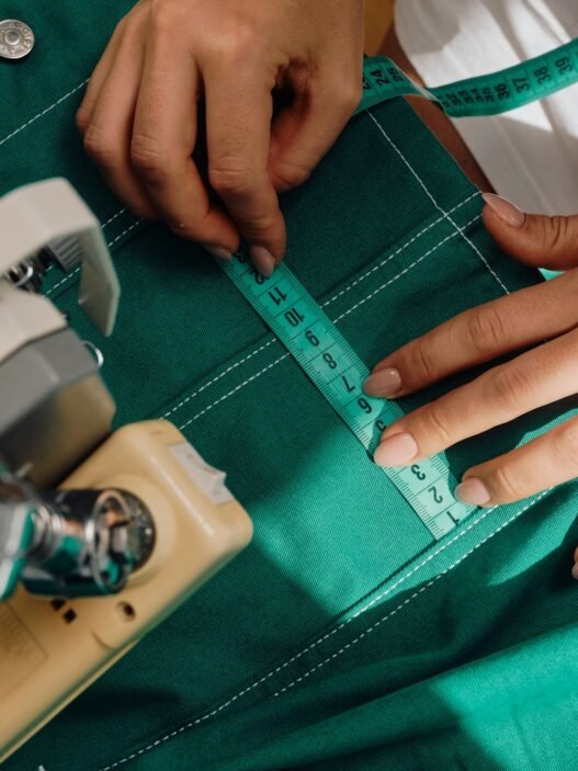 A person with a fabric measuring tape measuring a garment that they have in their sewing machine.