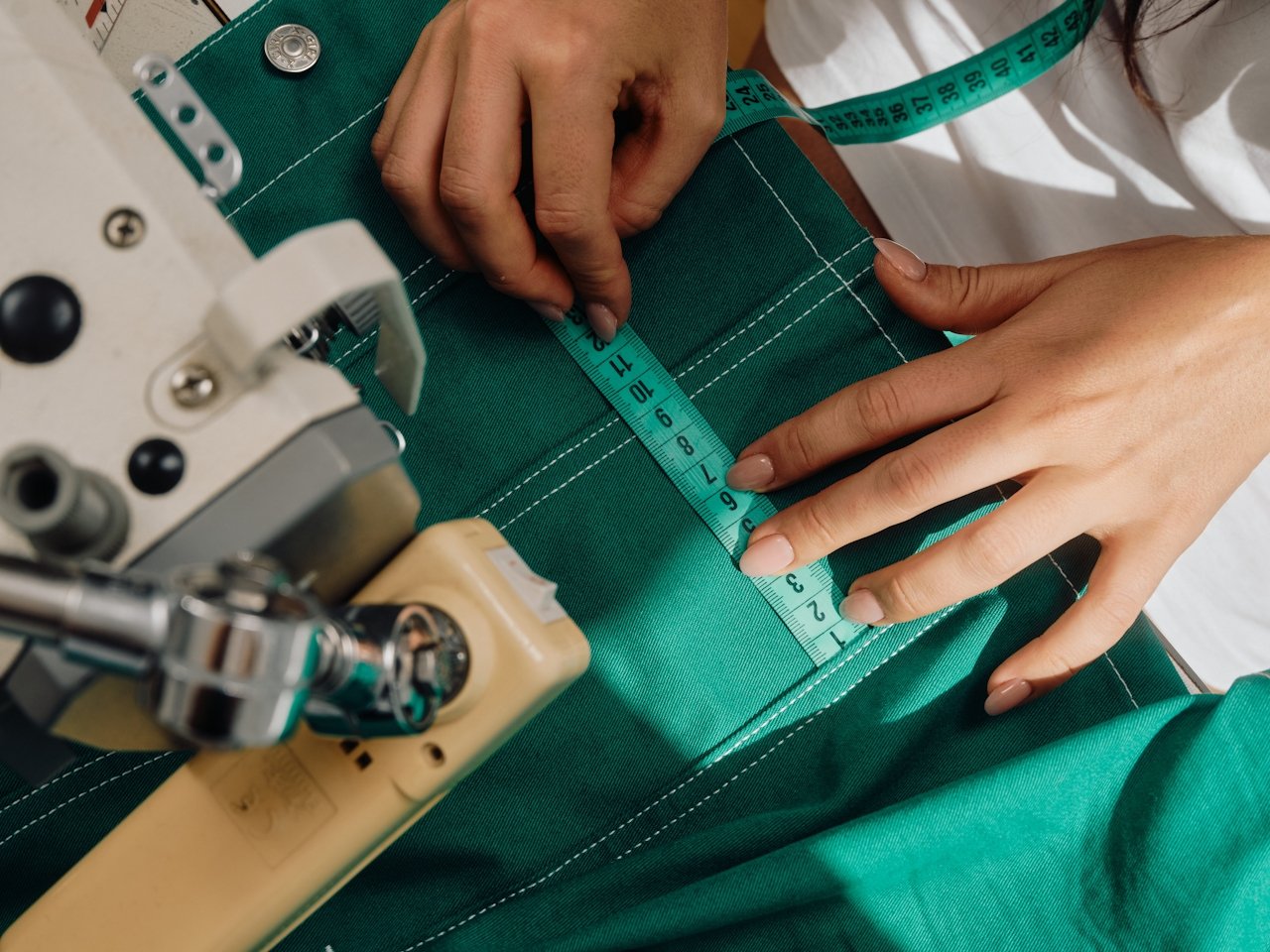 A person with a fabric measuring tape measuring a garment that they have in their sewing machine.