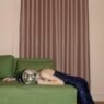 A person in a squint dress laying on a green couch with a disco covering her face.