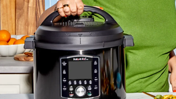 A women in a green sweater in her kitchen with her hand on the lid of an instant pot