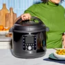 A women in a green sweater in her kitchen with her hand on the lid of an instant pot