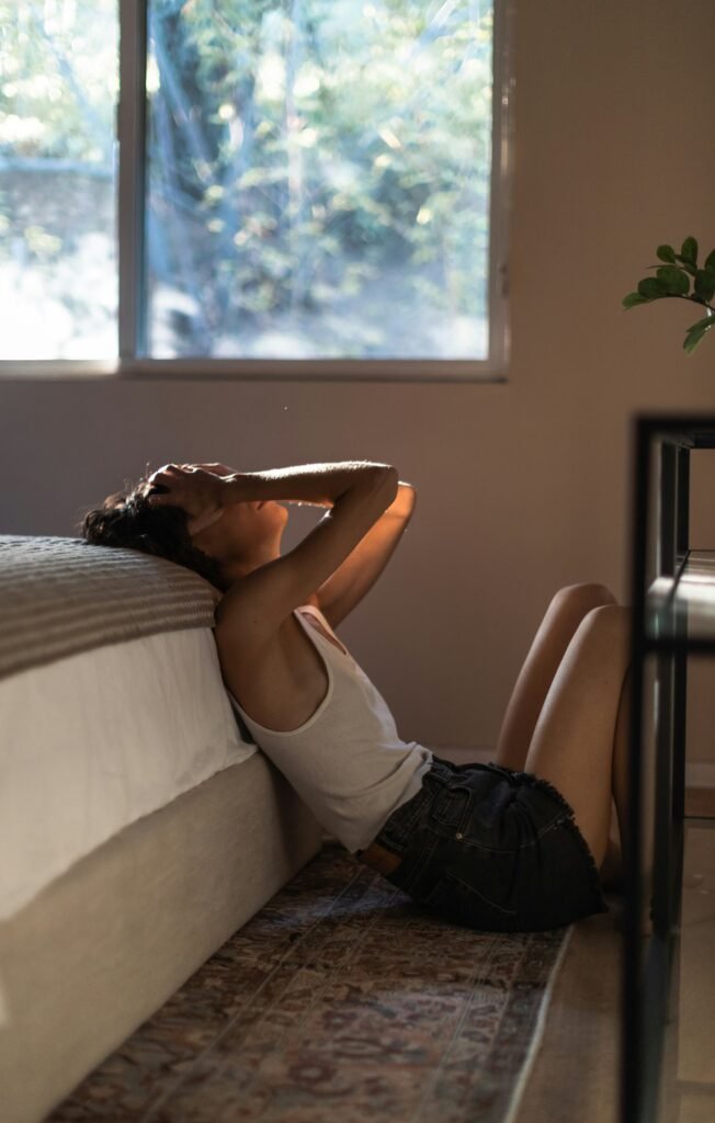 A women sits on the floor of her bedroom visibly upset.
