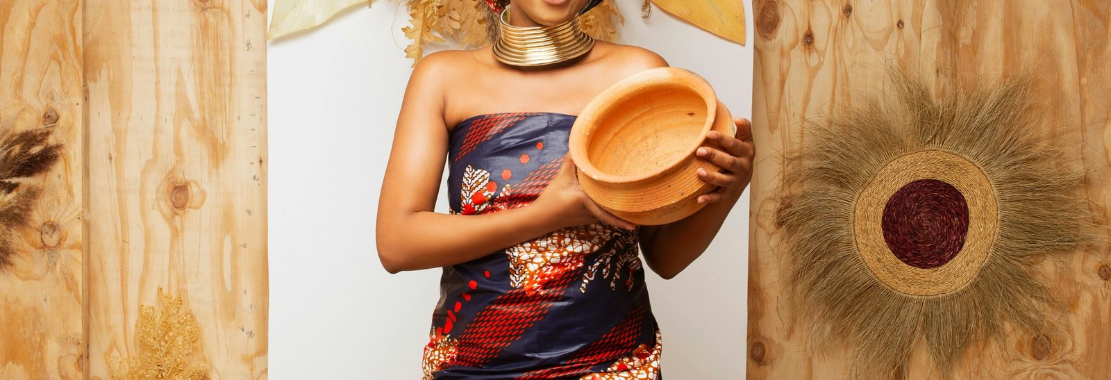 A black woman in traditional garb holding a handmade piece of pottery.