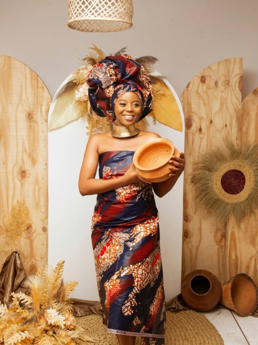 A black woman in traditional garb holding a handmade piece of pottery.