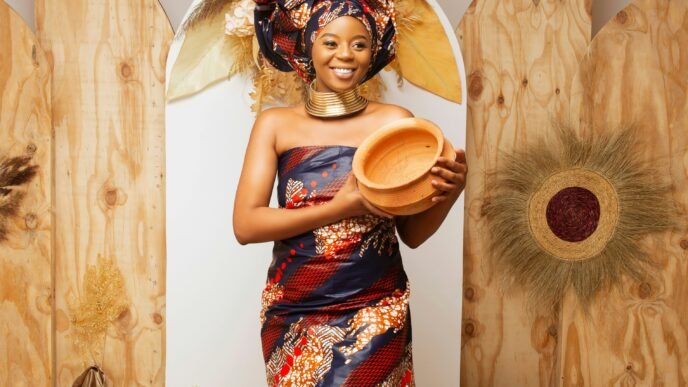 A black woman in traditional garb holding a handmade piece of pottery.