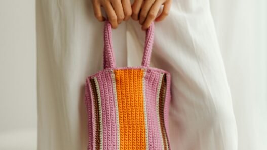 A woman in a long white dress holding an orange and purple striped crocheted purse.