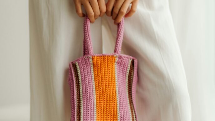 A woman in a long white dress holding an orange and purple striped crocheted purse.