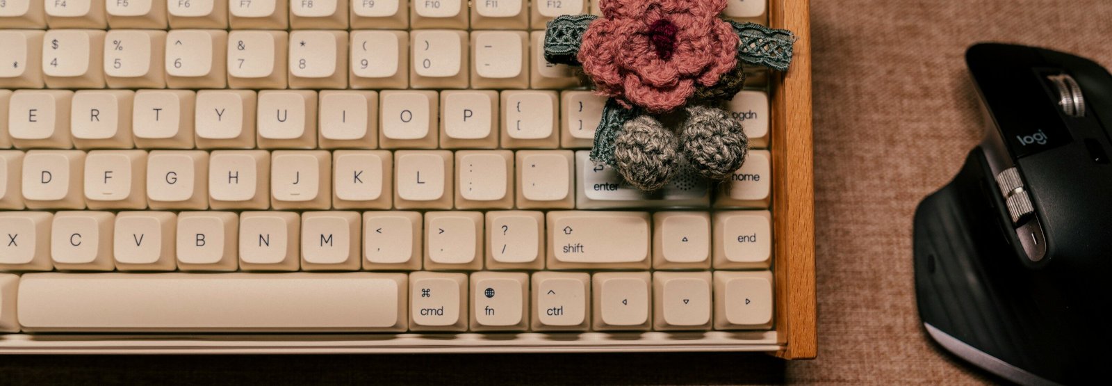 A pink crocheted blossom sitting on a vintage computer keyoard.