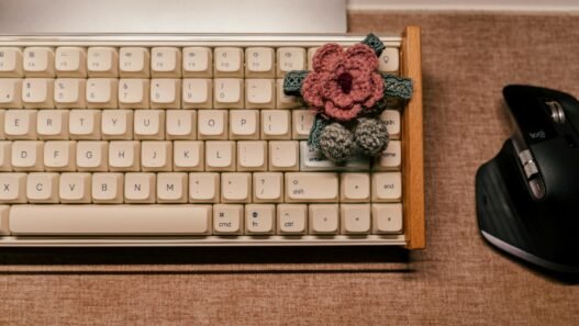 A pink crocheted blossom sitting on a vintage computer keyoard.