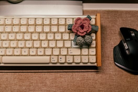 A pink crocheted blossom sitting on a vintage computer keyoard.