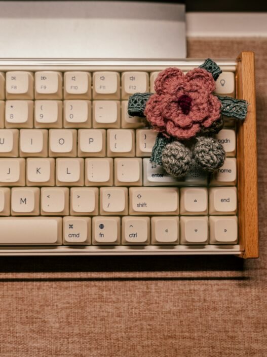A pink crocheted blossom sitting on a vintage computer keyoard.