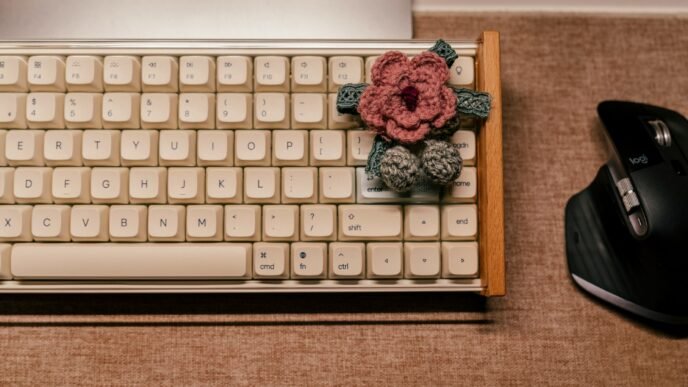 A pink crocheted blossom sitting on a vintage computer keyoard.