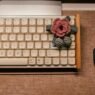 A pink crocheted blossom sitting on a vintage computer keyoard.